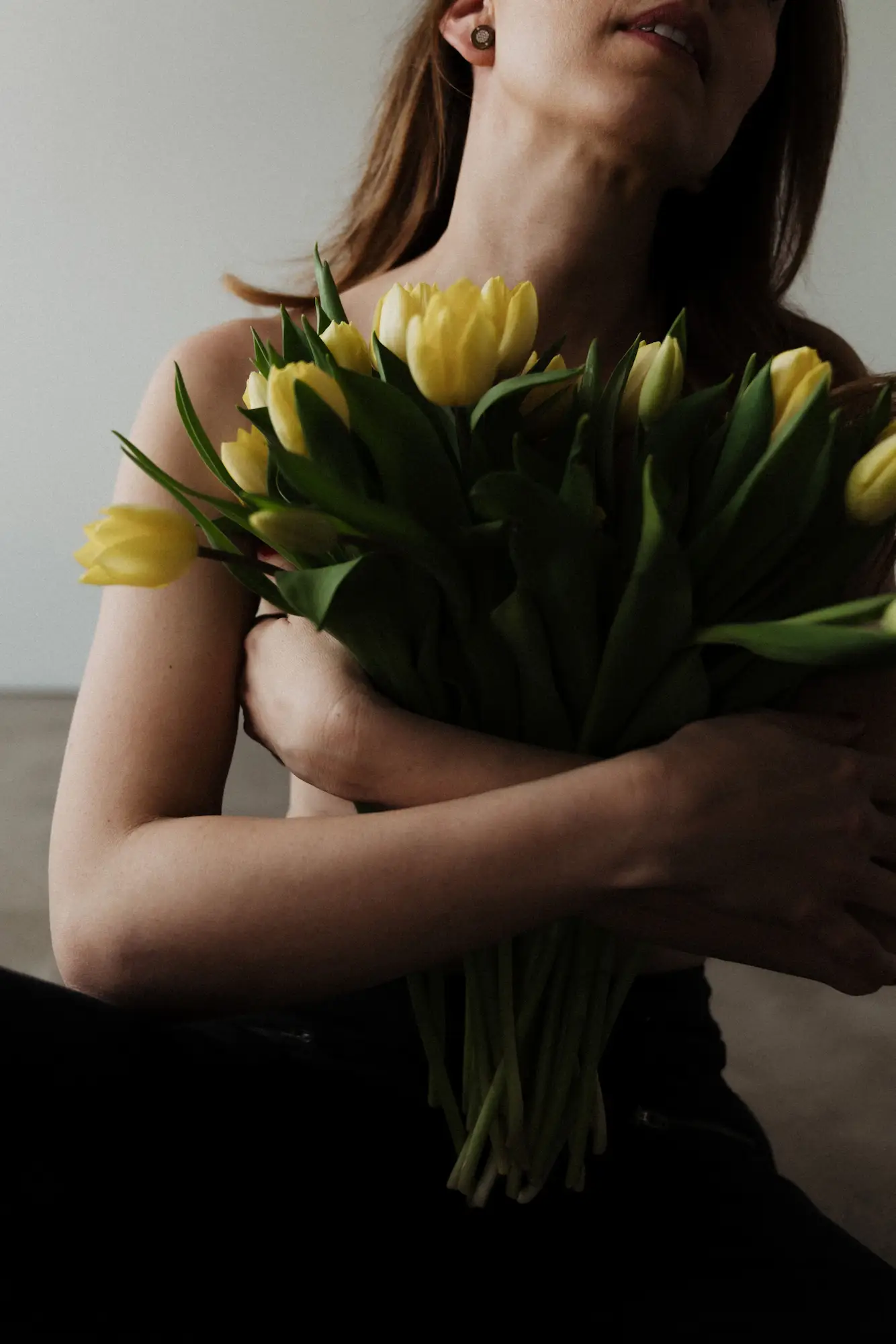 Žena s náručou žltých tulipánov v tmavom ateliéri