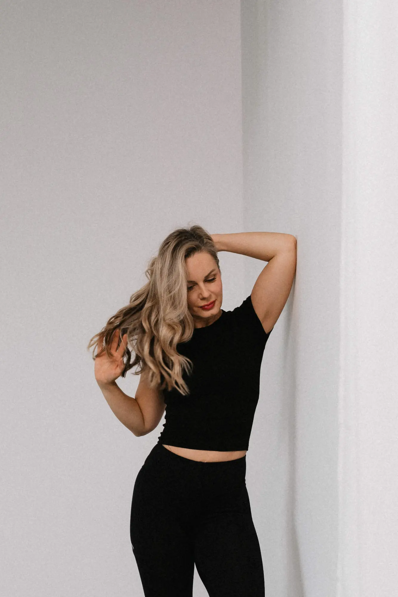 Blondínka v čiernom oblečení opretá o bielu stenu