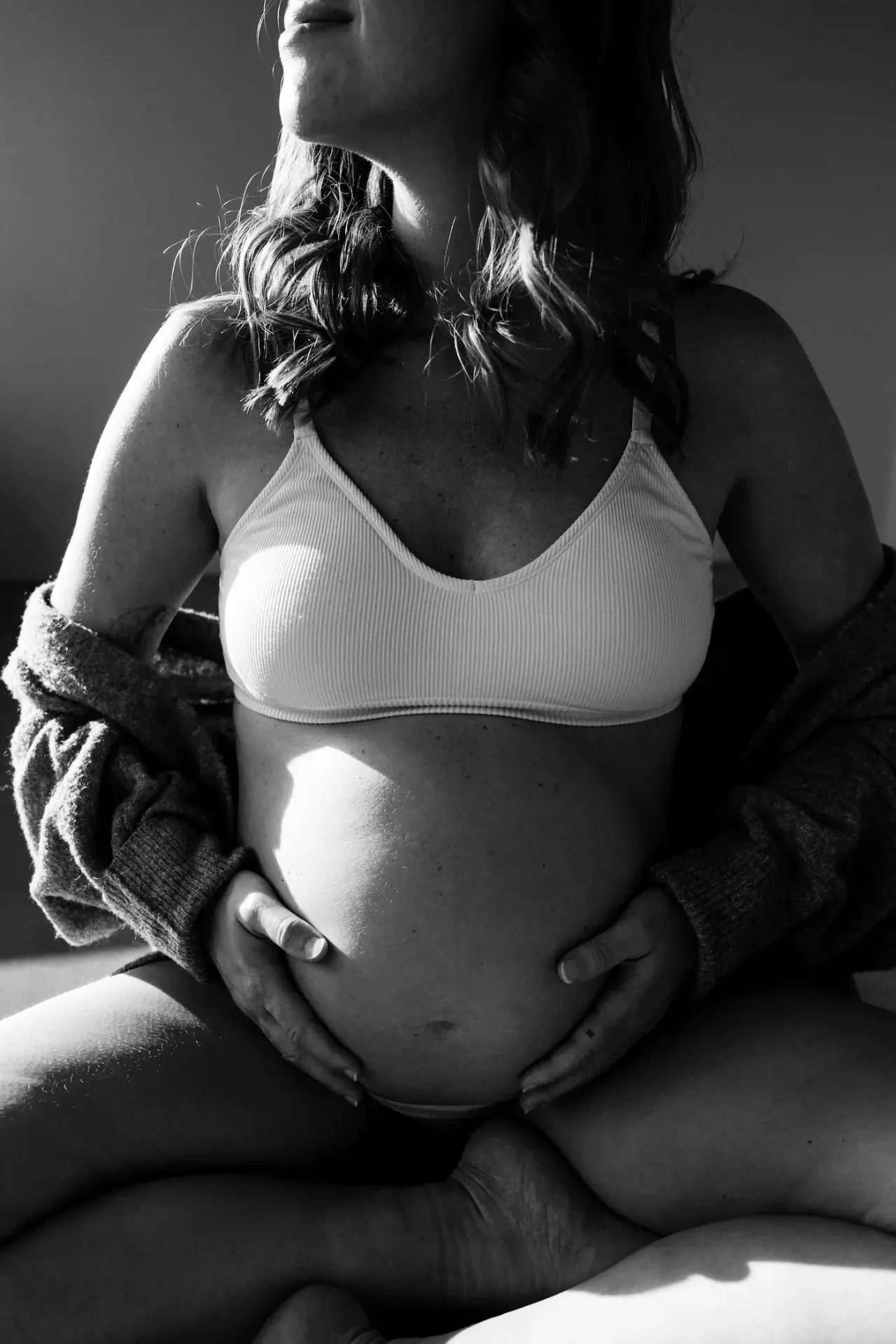 Tehotná žena držiaca si bruško v mäkkom bočnom svetle, čiernobiela fotografia