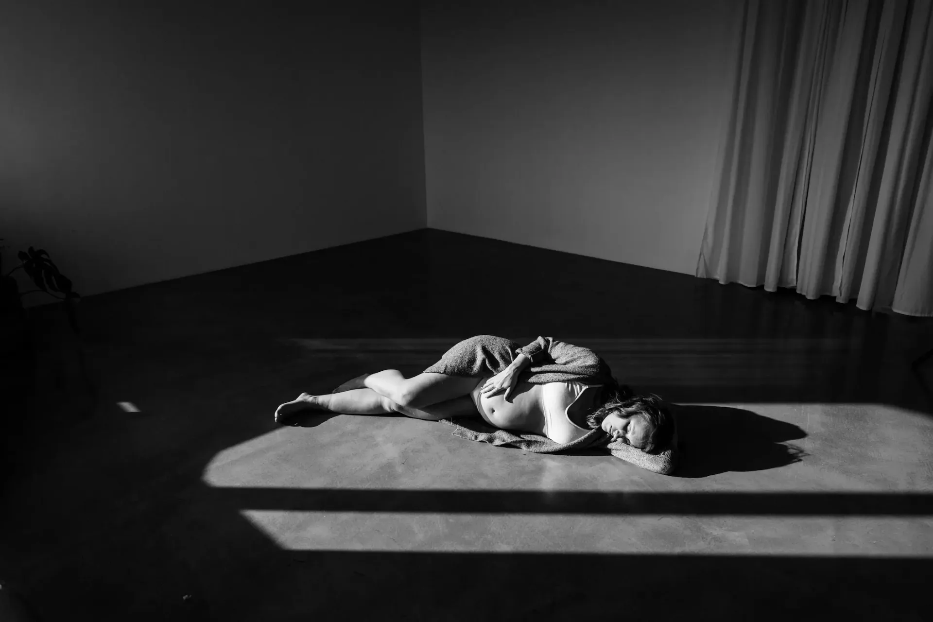 Tehotná žena ležiaca v páse svetla na podlahe štúdia, čiernobiela fotografia
